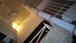 Um quarto com piso ladrilhado, cama com cabeceira branca e janela com vista para o exterior.