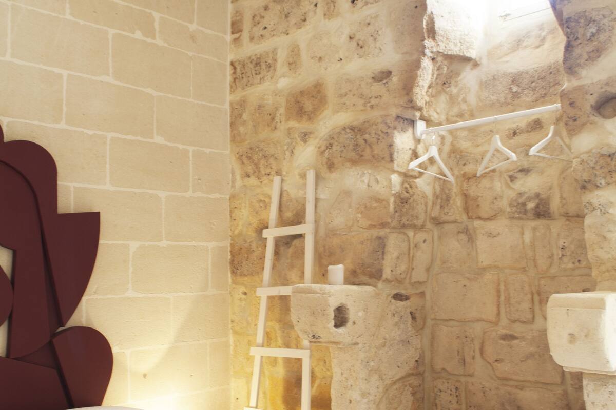A bedroom with a brick wall, a window with a view, a bed, a small bedside table, and a nightstand.