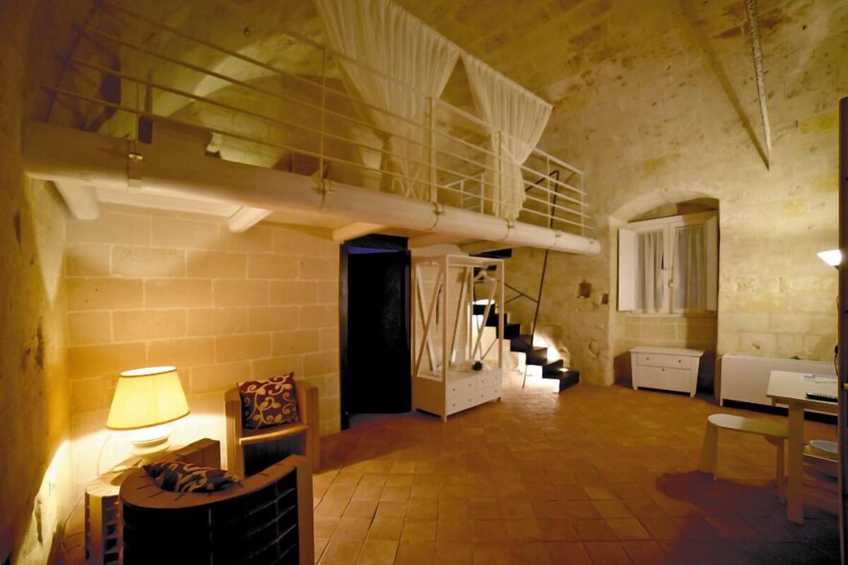 A spacious room with a high ceiling, a staircase, and a bed.