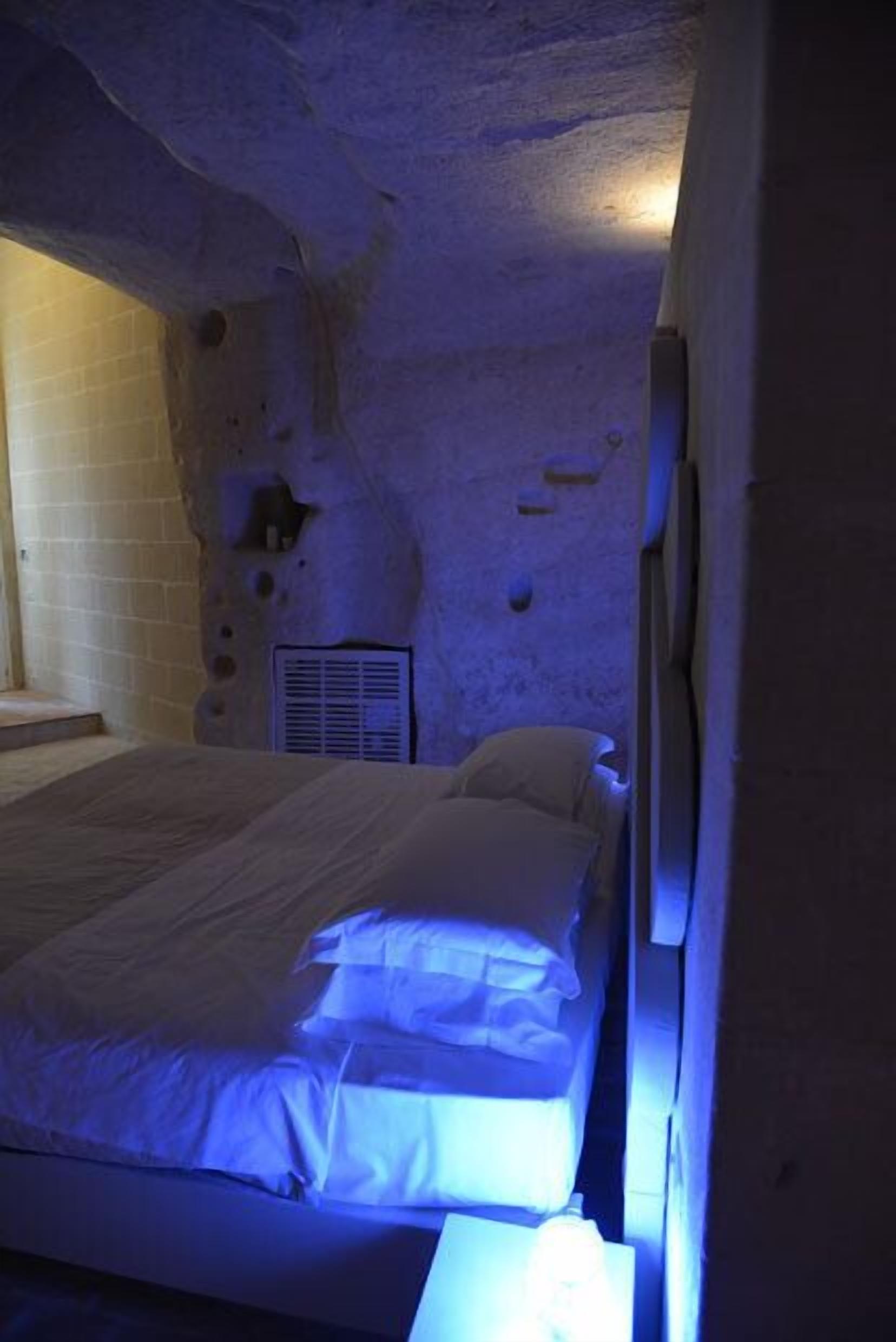 Una camera da letto con parete in pietra, un letto con biancheria bianca e una bocchetta d'aria sulla parete.
