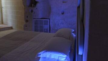 Una camera da letto con parete in pietra, un letto con biancheria bianca e una bocchetta d'aria sulla parete.