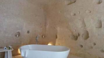Un baño con una bañera independiente, una mesita de noche con artículos de aseo y una pared con textura.