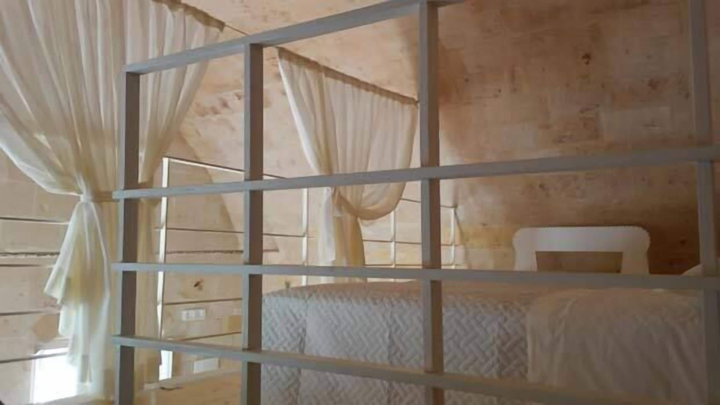 Une chambre avec un lit en métal, un matelas blanc et un rideau.