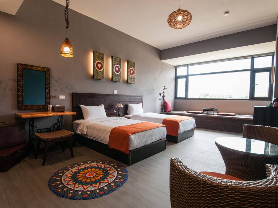 Habitación de hotel moderna con una cama grande, un escritorio pequeño, una mesa redonda, sillas de mimbre y un ventanal con vistas.