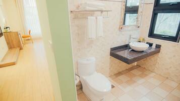A bathroom with a toilet, sink, and towel rack. There is a chair and a window in the adjacent room.