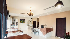 A modern dining area with a wooden table and white chairs, a kitchen in the background, and a reception desk with a wooden counter. - Zai Yan-Yan B&B (Ji'an)