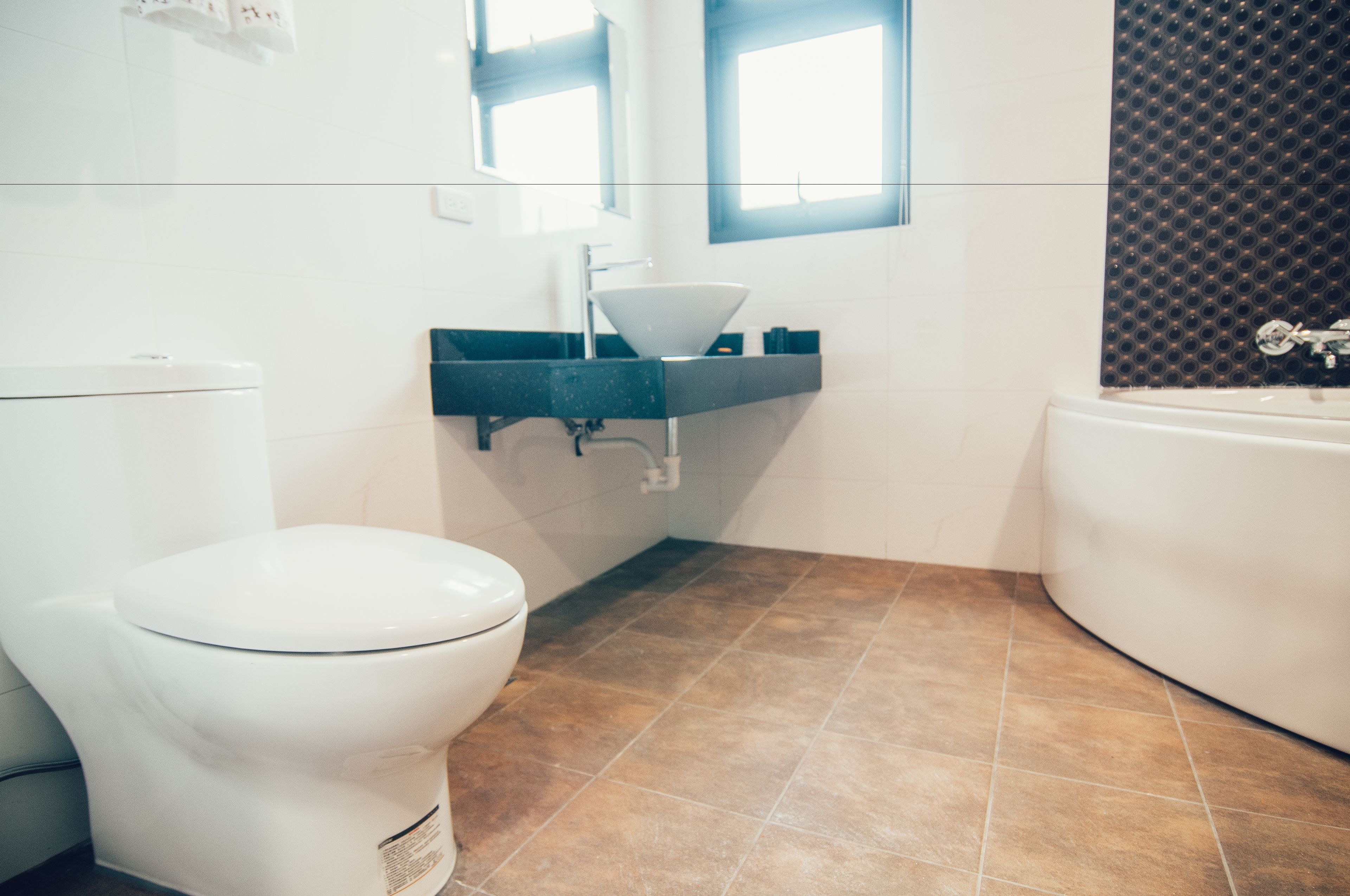 Un baño moderno con inodoro blanco, lavabo negro y bañera.