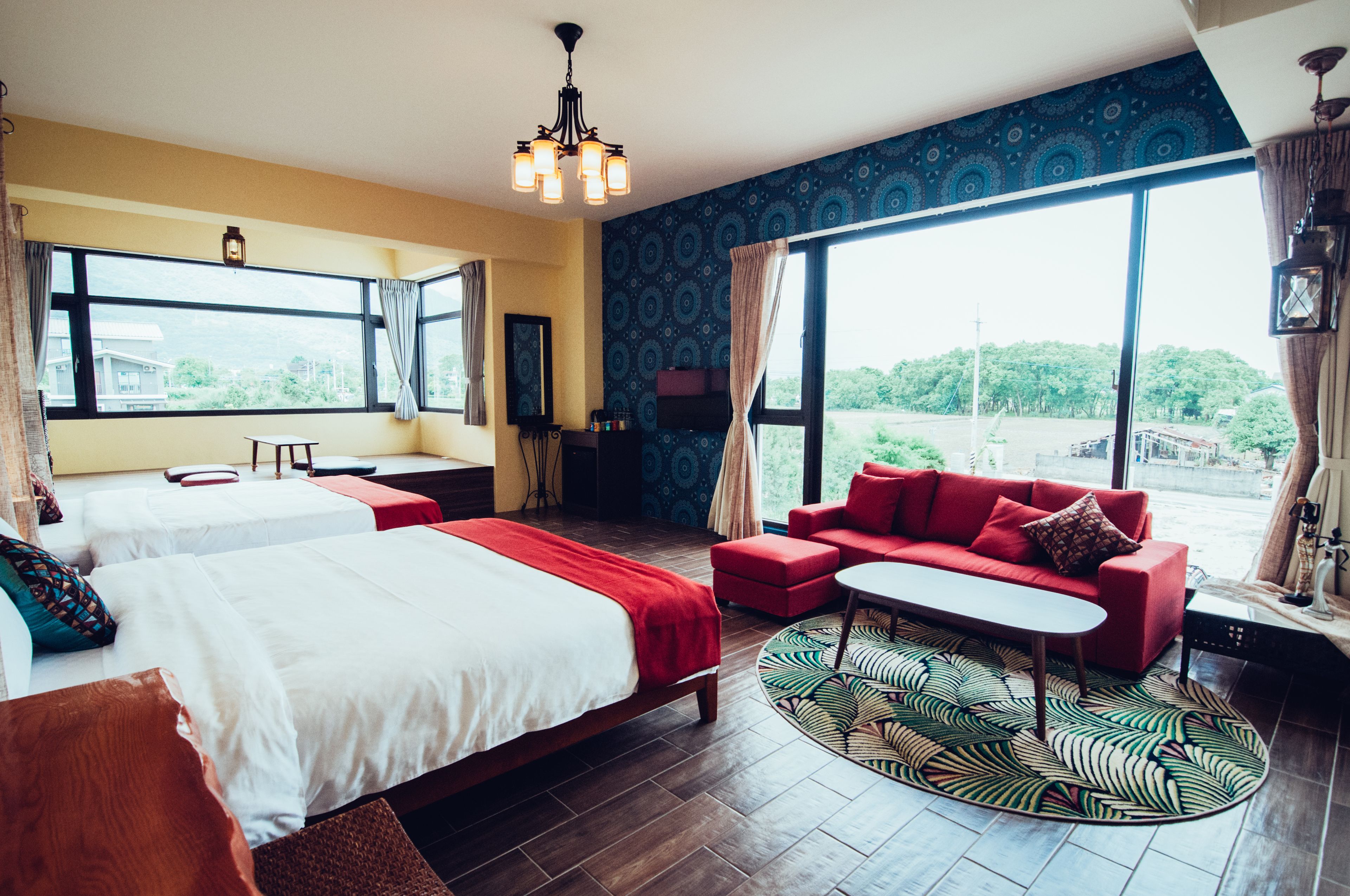 Habitación de hotel con dos camas, un sofá rojo, una mesita y ventanas amplias que dan a zonas verdes.