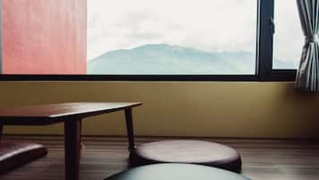 Una habitación con una mesa de madera y dos taburetes redondos, una ventana con vistas a montañas y una cortina.