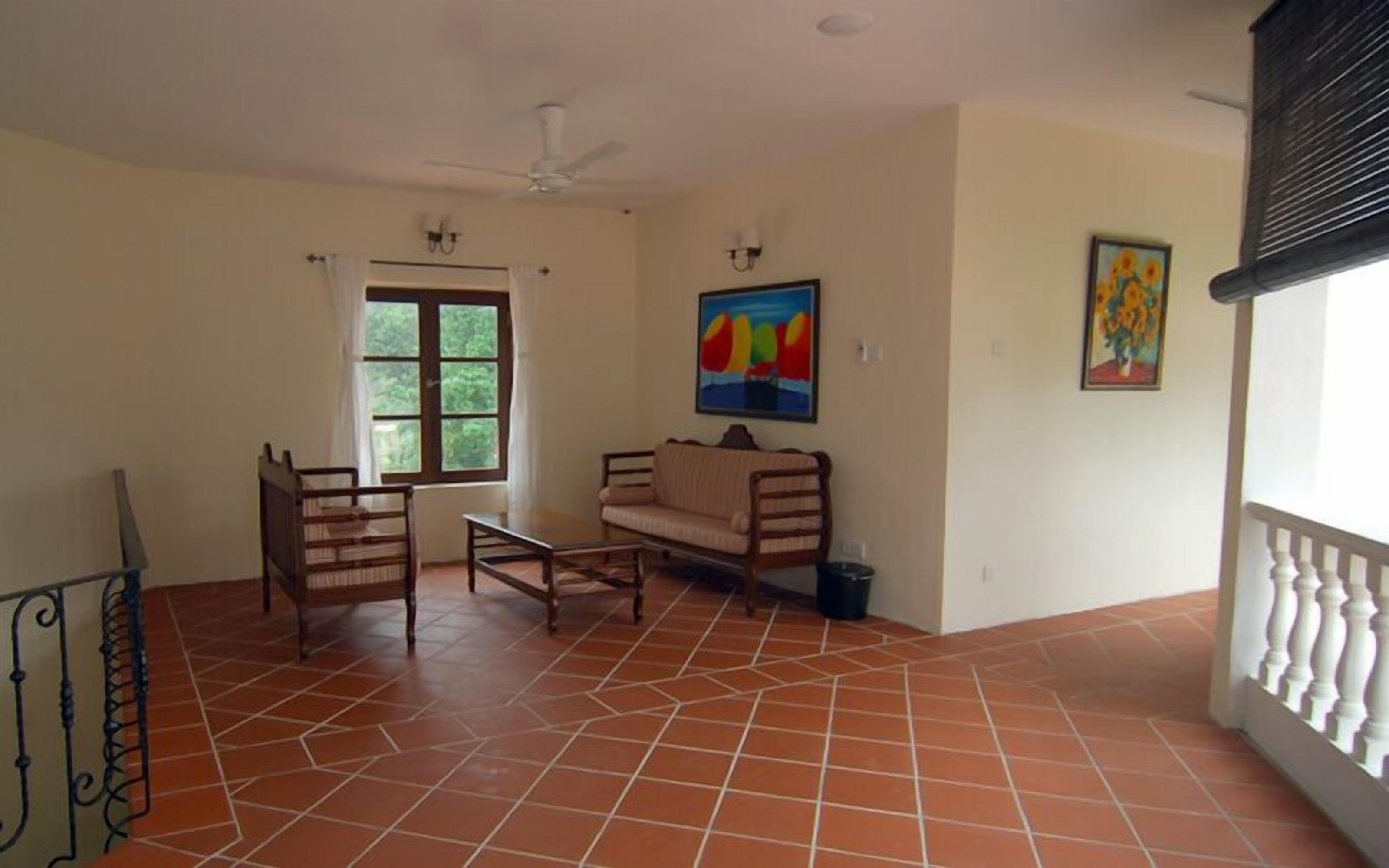 A spacious living area with a tiled floor, a ceiling fan, a sofa, a coffee table, and a window with curtains.