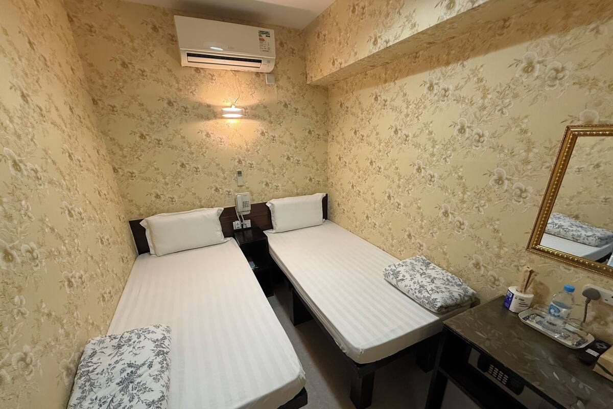 Une chambre avec deux lits simples, une petite table avec un miroir et un appareil de climatisation fixé au mur.
