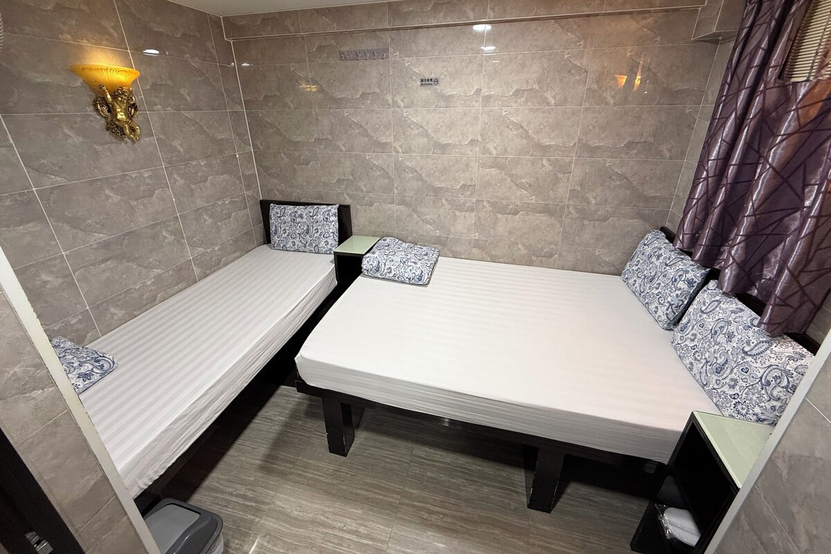 Una habitación pequeña y funcional con dos camas individuales, una mesita y una lámpara fijada a la pared.
