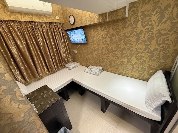 Una cama individual con televisor, cortinas y un papel tapiz estampado en una habitación.
