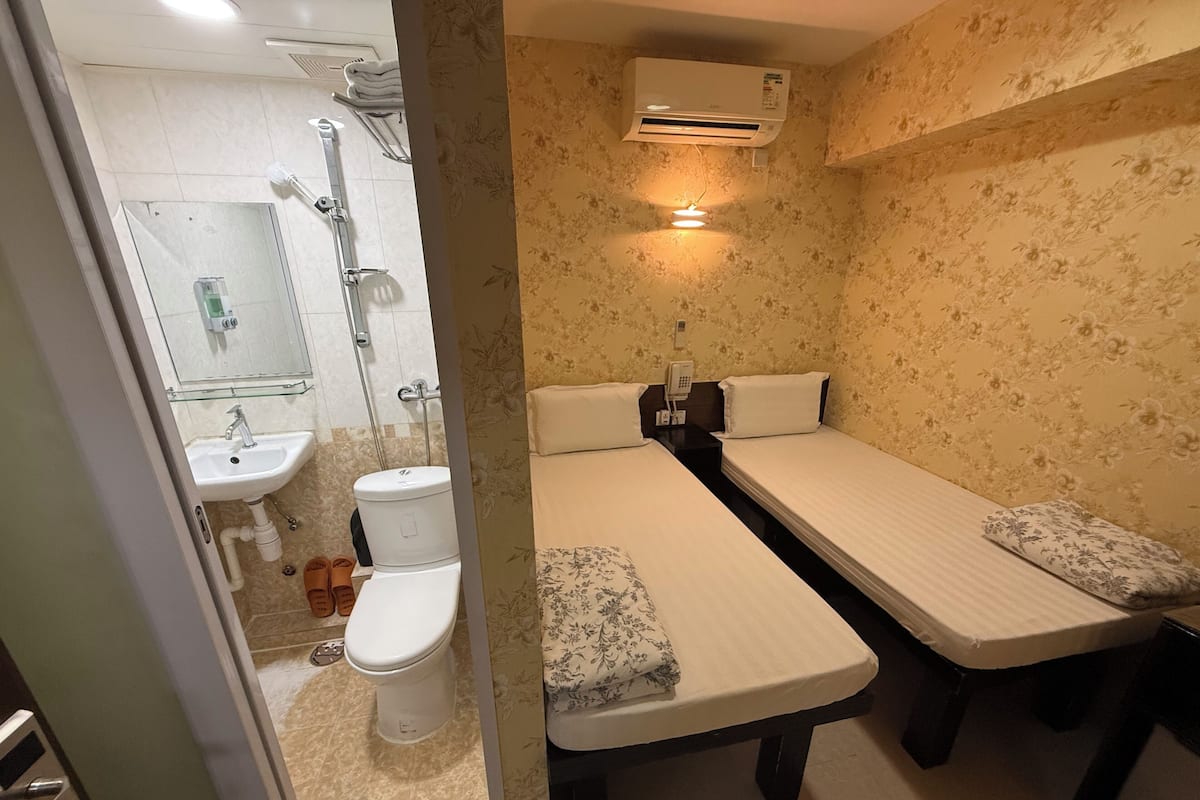 Un baño con inodoro, lavamanos, ducha y dos camas con almohadas.