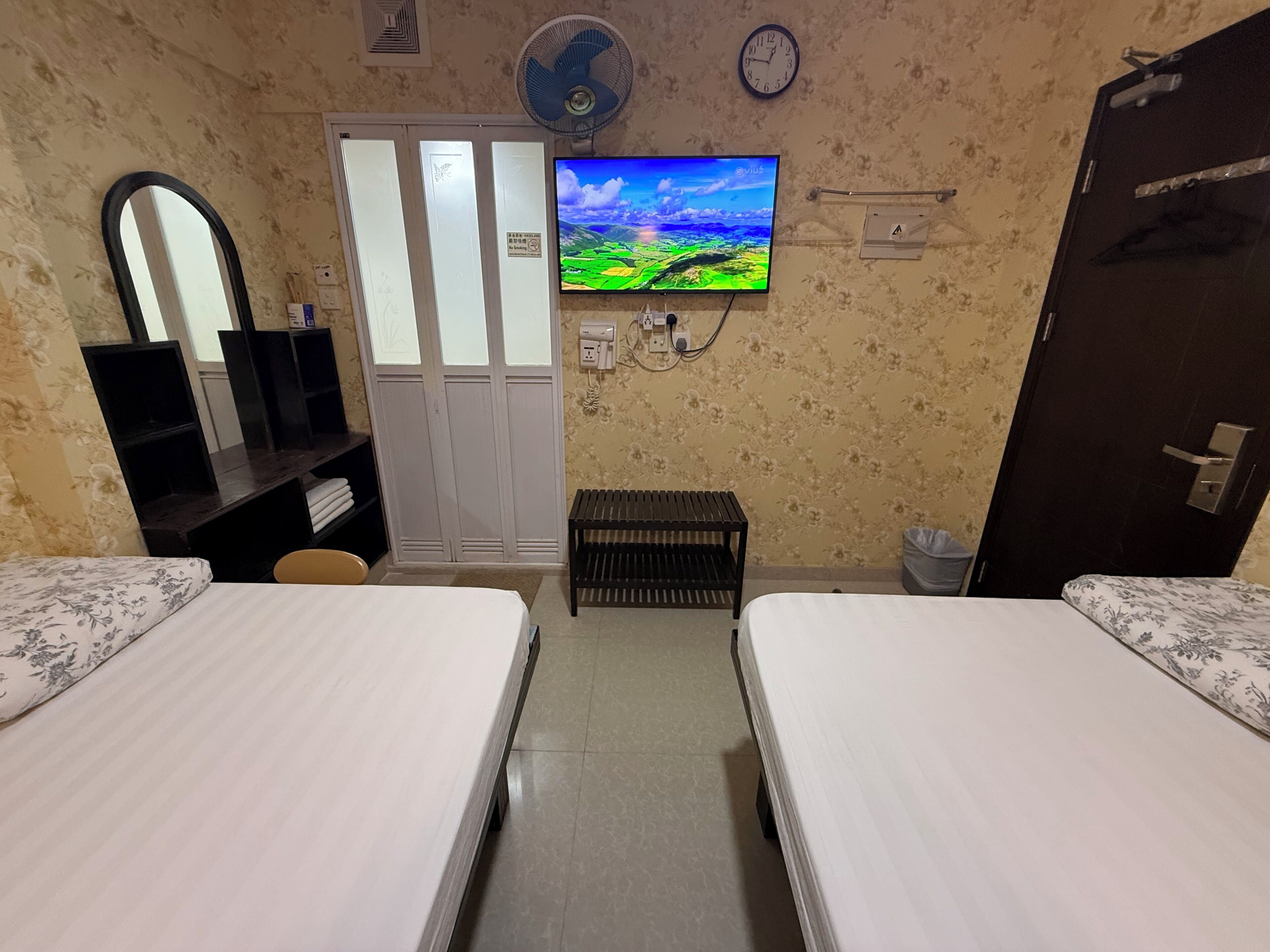 A hotel room with two beds, a TV, a wardrobe, a mirror, and a small bench.