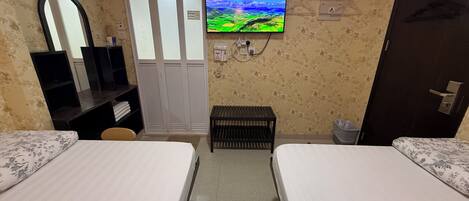 A hotel room with two beds, a TV, a wardrobe, a mirror, and a small bench.
