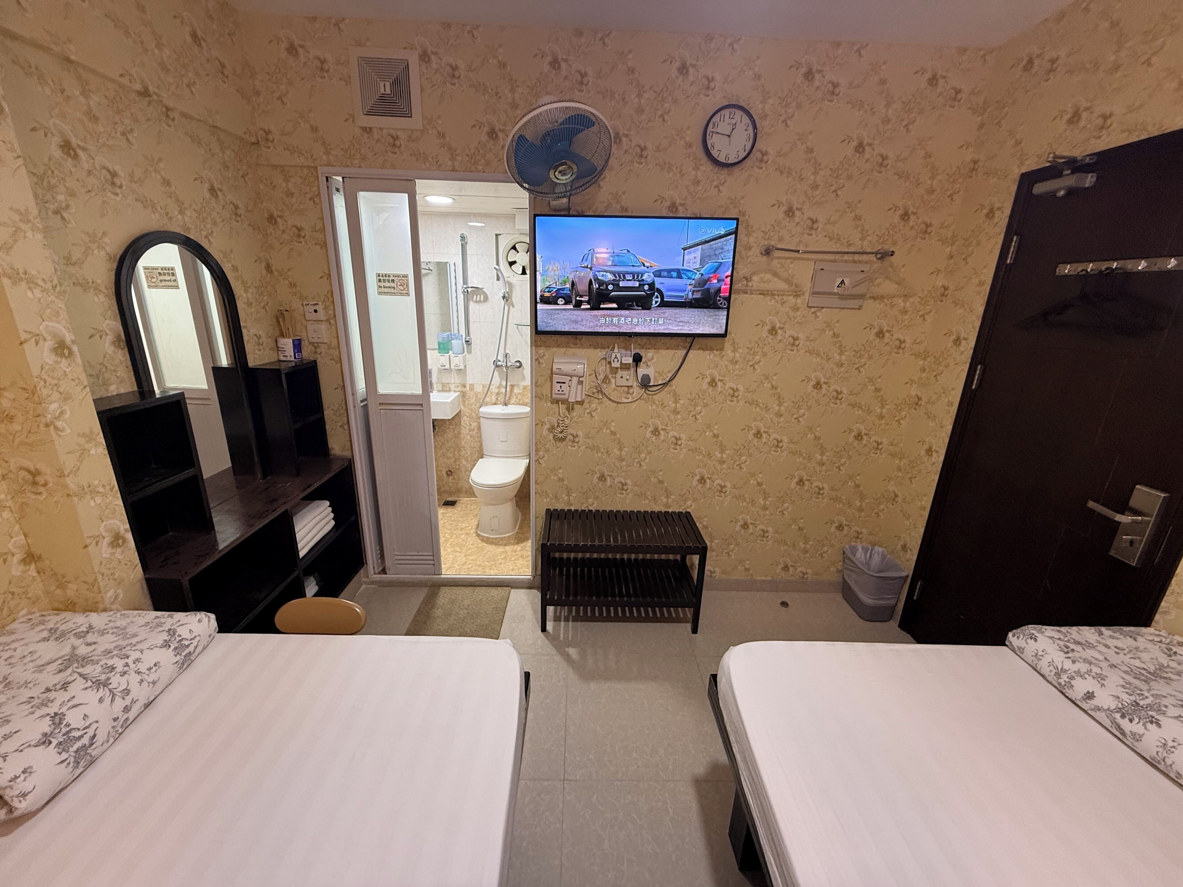 Une chambre d’hôtel avec deux lits, une télévision, un miroir, une porte et une salle de bain visible à travers une porte ouverte.