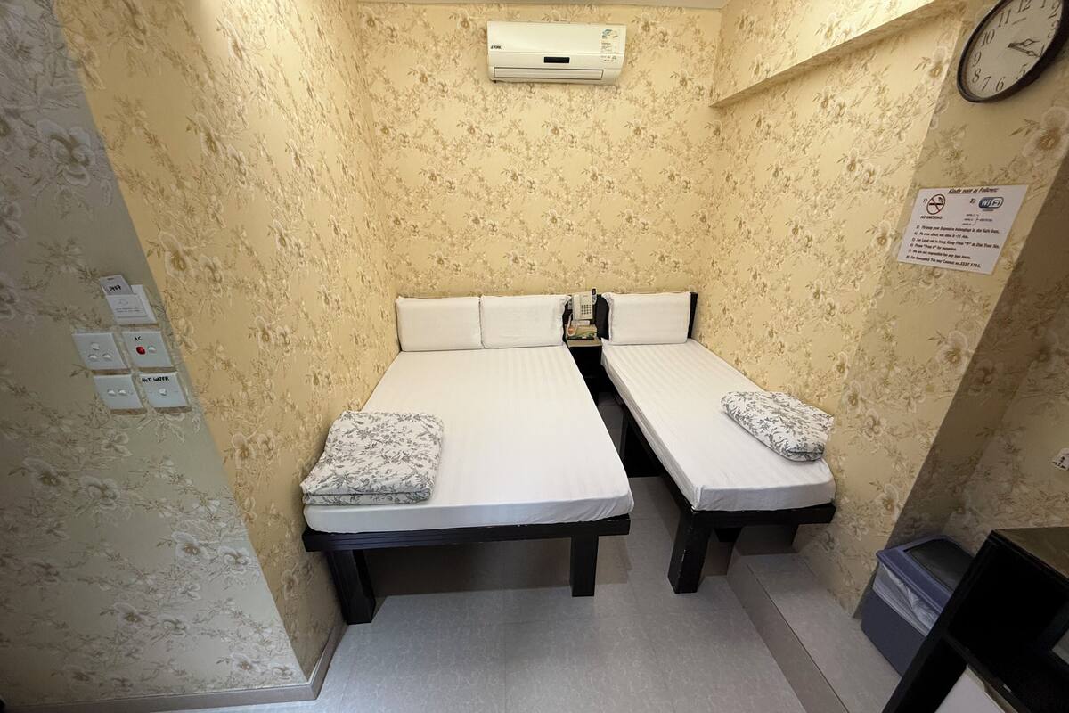 Une petite chambre avec deux lits simples, un climatiseur fixé au mur, une horloge et un panneau indiquant les informations relatives au Wi-Fi.