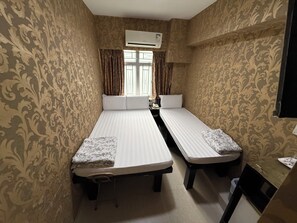 Een kamer met twee eenpersoonsbedden, een tafeltje, een stoel, een airconditioning en een raam met gordijnen.