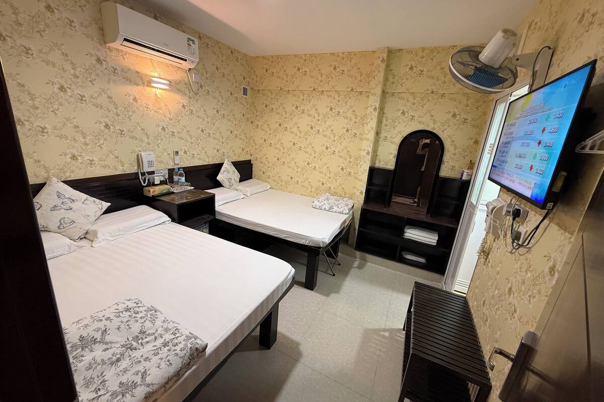 Une chambre d’hôtel avec deux lits, un bureau, une chaise, une télévision, un climatiseur et un ventilateur.