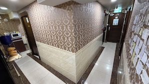 Un hall de hotel con papel tapiz estampado, piso de baldosas, microondas, un osito de peluche y un tablón de anuncios.