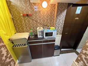 Een compacte hotelkamer met een kitchenette, een kleine prullenbak, een waterdispenser en een magnetron op het aanrecht.