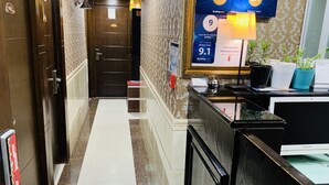 Zona de recepción de hotel con piso de mármol, mostrador de recepción, una pantalla mostrando premios y una puerta con un cartel.