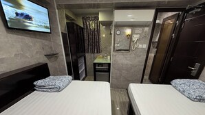 Una habitación de hotel con dos camas, televisor, baño con ducha y retrete.