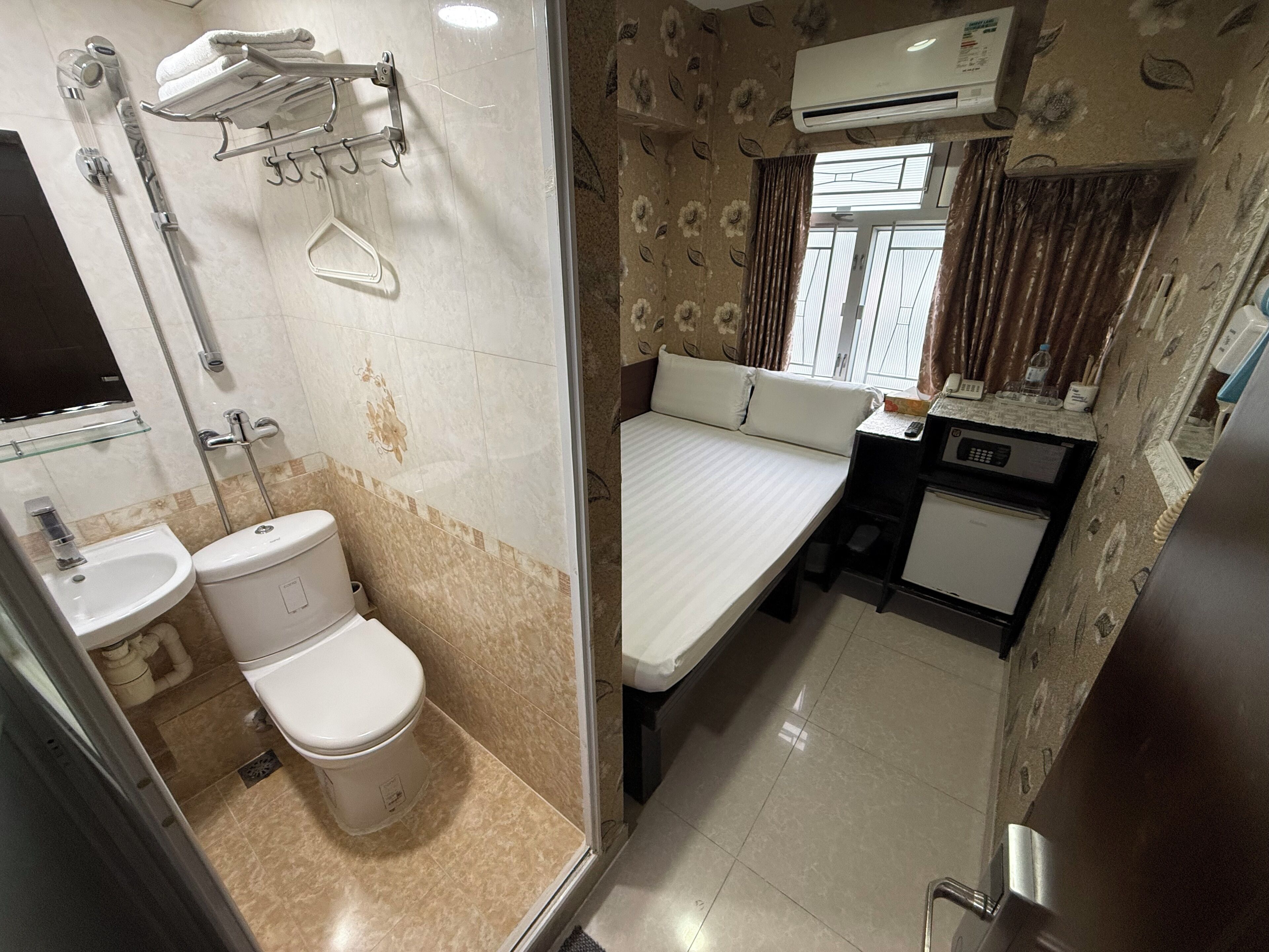 A compact hotel room with a shower, toilet, sink, bed, and a small kitchenette.