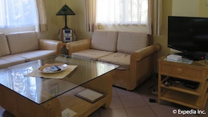 Una sala de estar con sofá, una mesa de centro de vidrio, televisor y lámpara.