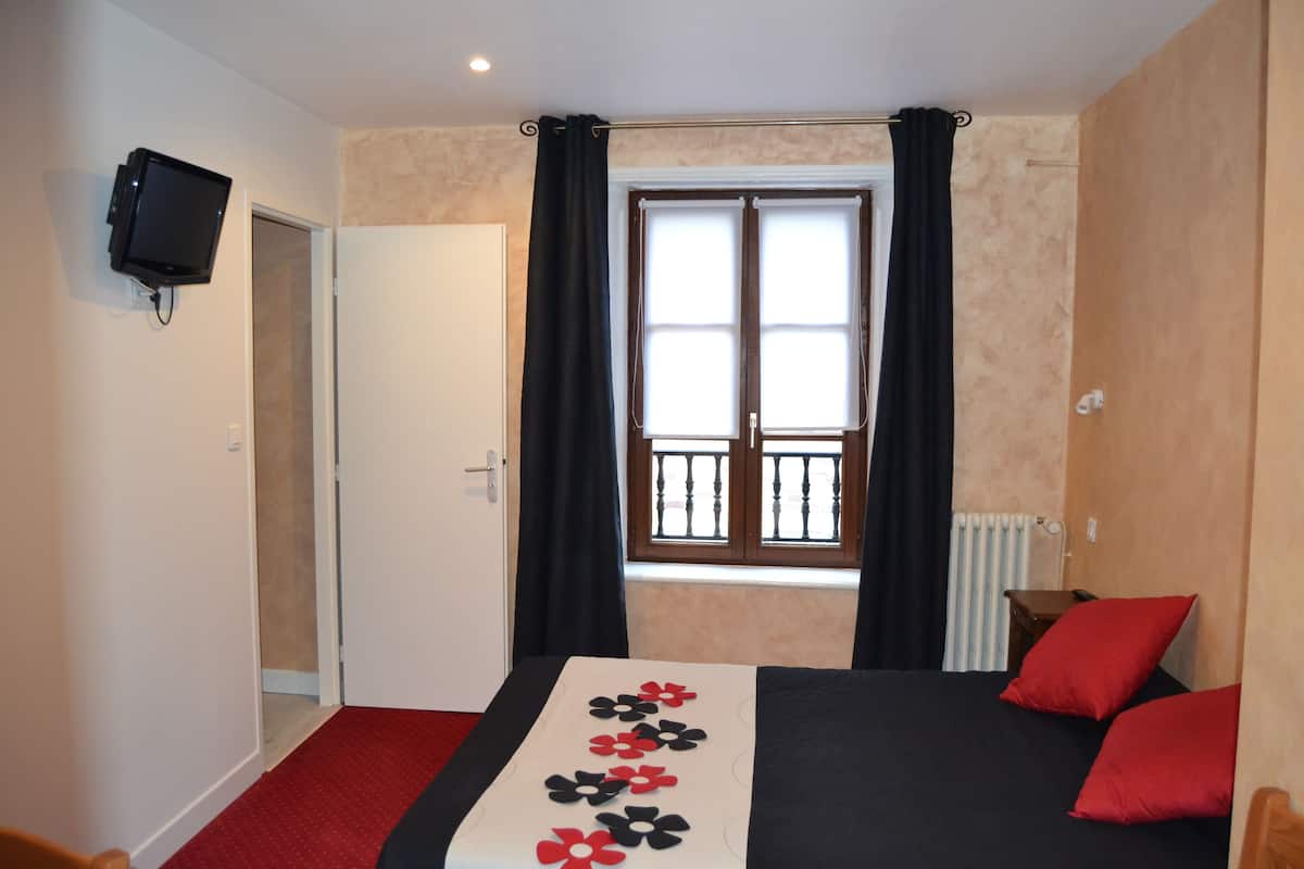 Habitación de hotel con cama, televisor montado en la pared, ventana con cortinas y radiador.