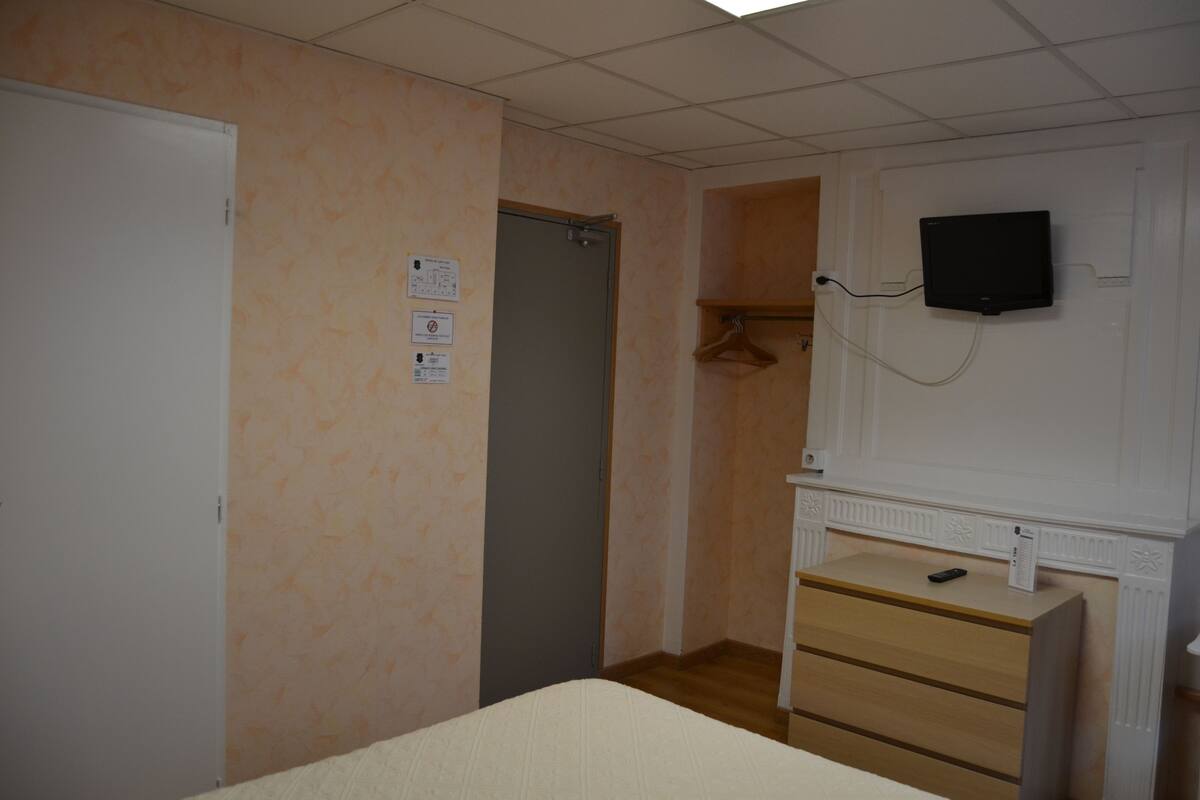 Una habitación con cama, cómoda, televisor montado en la pared y una puerta.