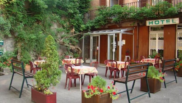 Een terras met tafels en stoelen, omgeven door groen en een houten gebouw met een 'HOTEL' bord.