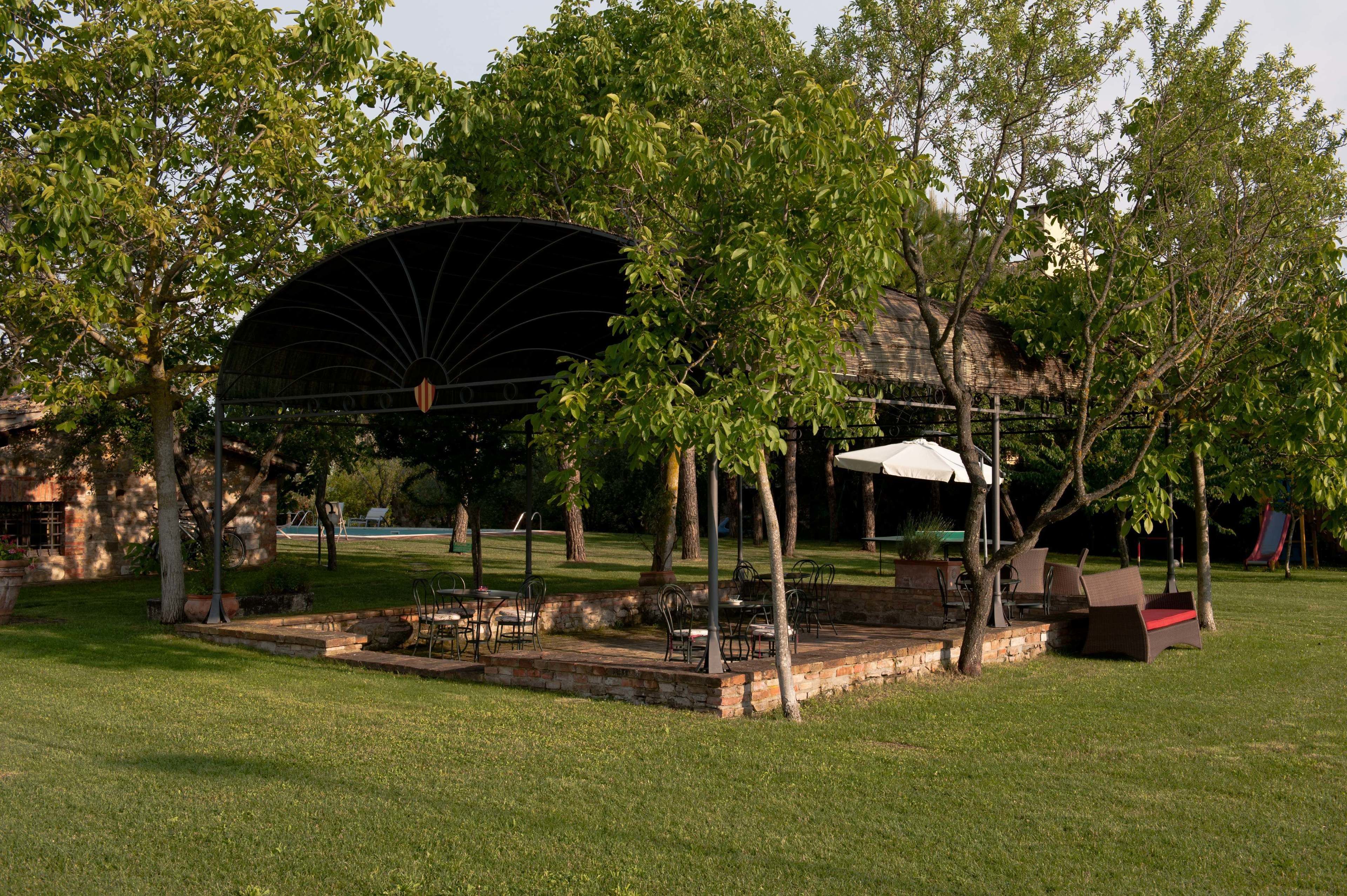 An outdoor patio area with a covered seating area, surrounded by trees and a grassy lawn.