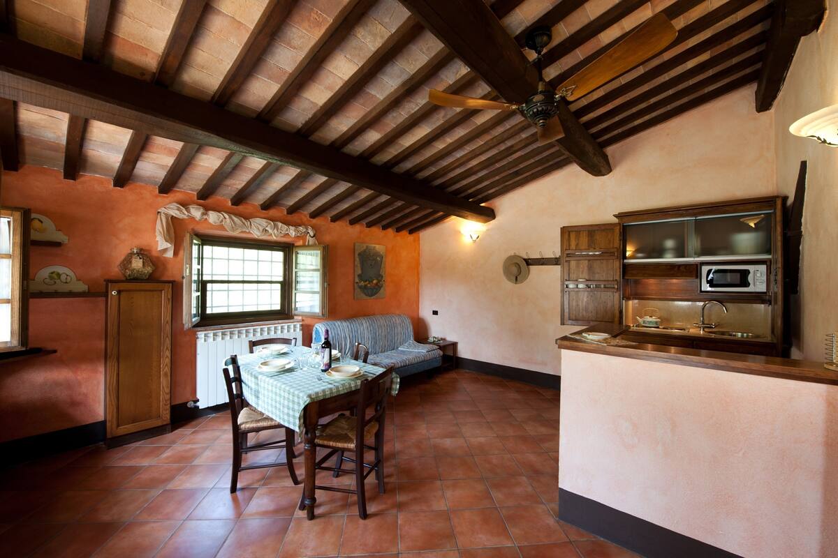 Una cocina rústica con techo de madera, una mesa de comedor con sillas, horno empotrado y ventana con vistas.