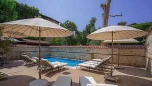 Un área junto a la piscina con sillones de descanso y sombrillas, una piscina y una pared de piedra.