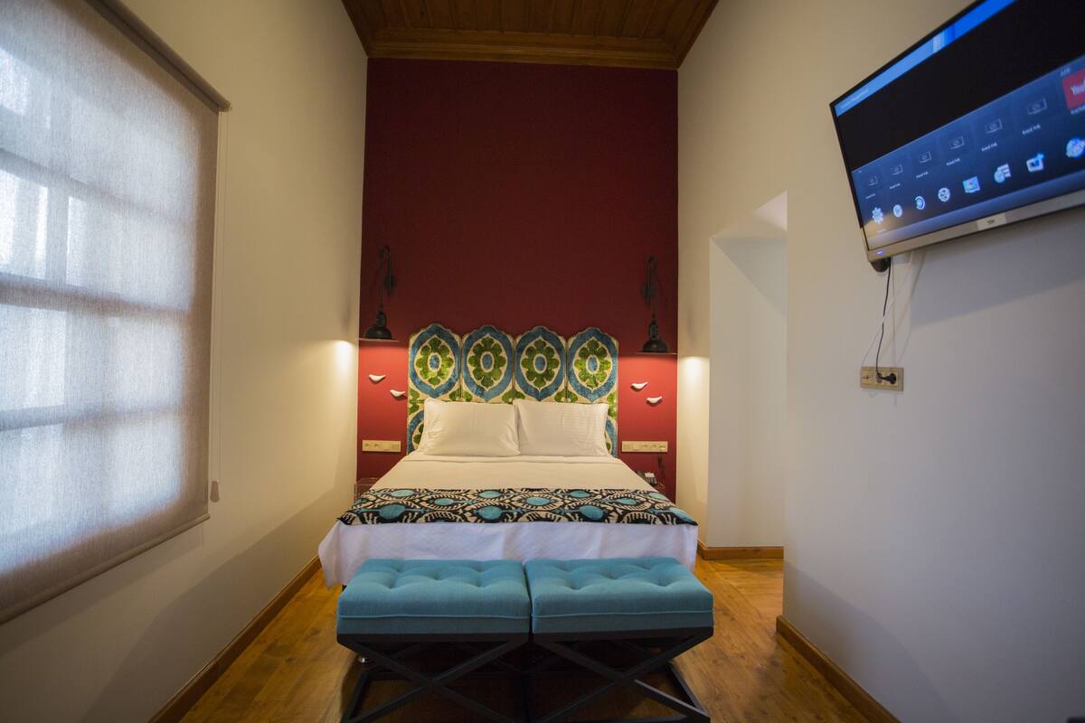Ein Schlafzimmer mit einem Bett, einem an der Wand montierten Fernseher und einem Fenster mit Jalousien.