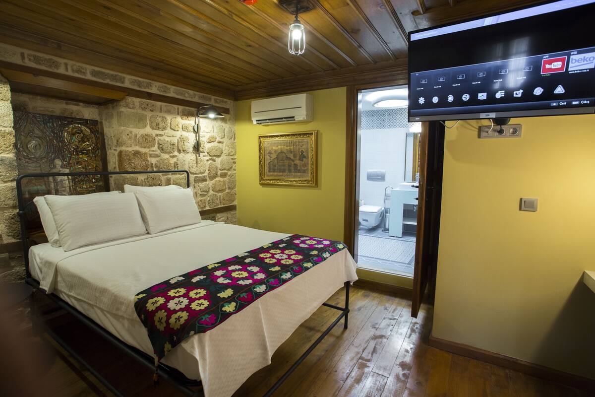 Ein Zimmer mit einem Bett, einem Fernseher, einer Steinsäule und einer Tür zu einem Badezimmer.
