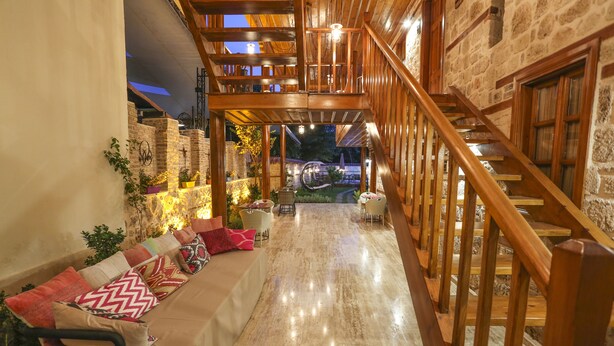 A wooden staircase leading to a second floor, a covered outdoor seating area with cushions, and a stone wall with plants. - Charme Hotel (Antalya)