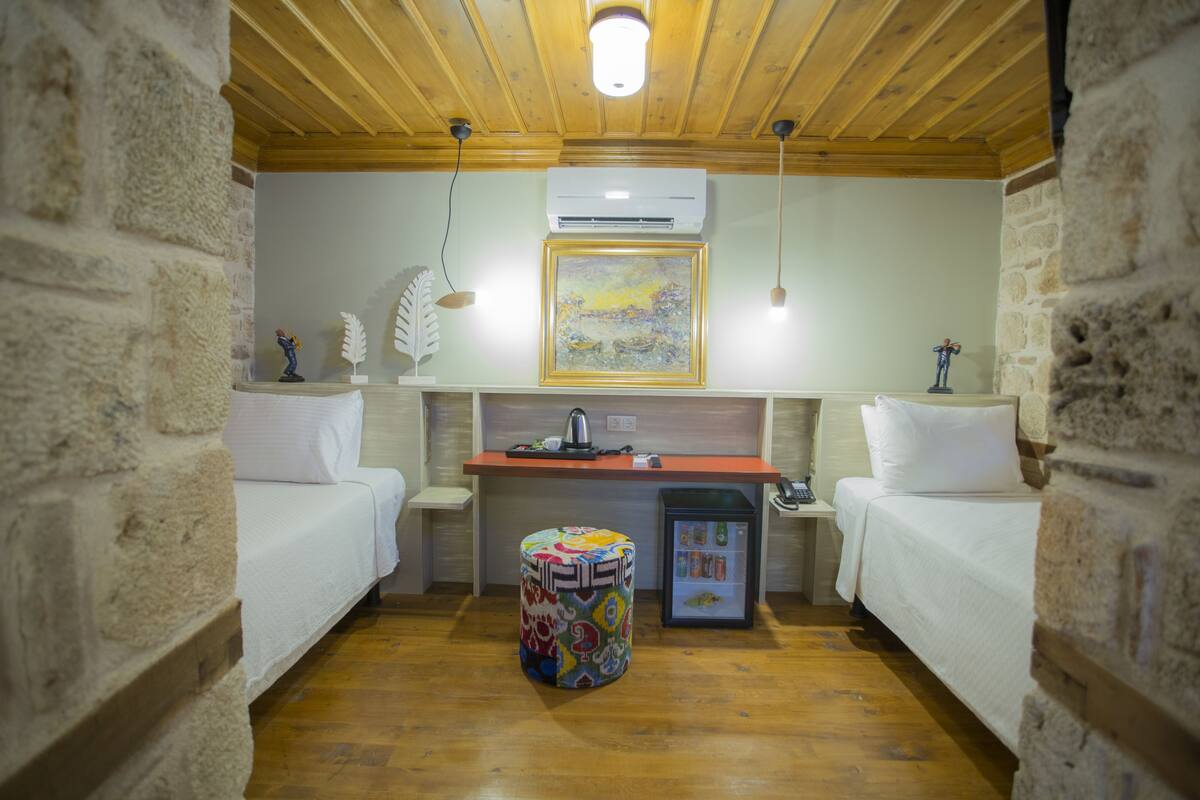 Ein gemütliches Zimmer mit zwei Betten, einem kleinen Tisch, einem Kühlschrank und einem farbenfrohen Hocker.