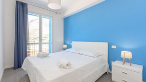 Een slaapkamer met een bed, twee nachtkastjes, een raam met gordijnen en uitzicht op het omliggende landschap.