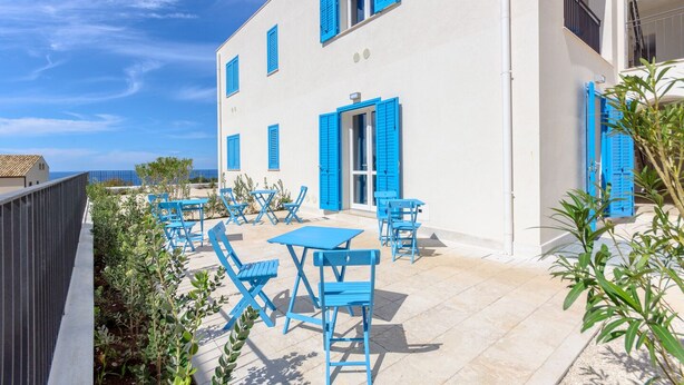 Een wit gebouw met blauwe luiken en een balkon met blauwe meubels.