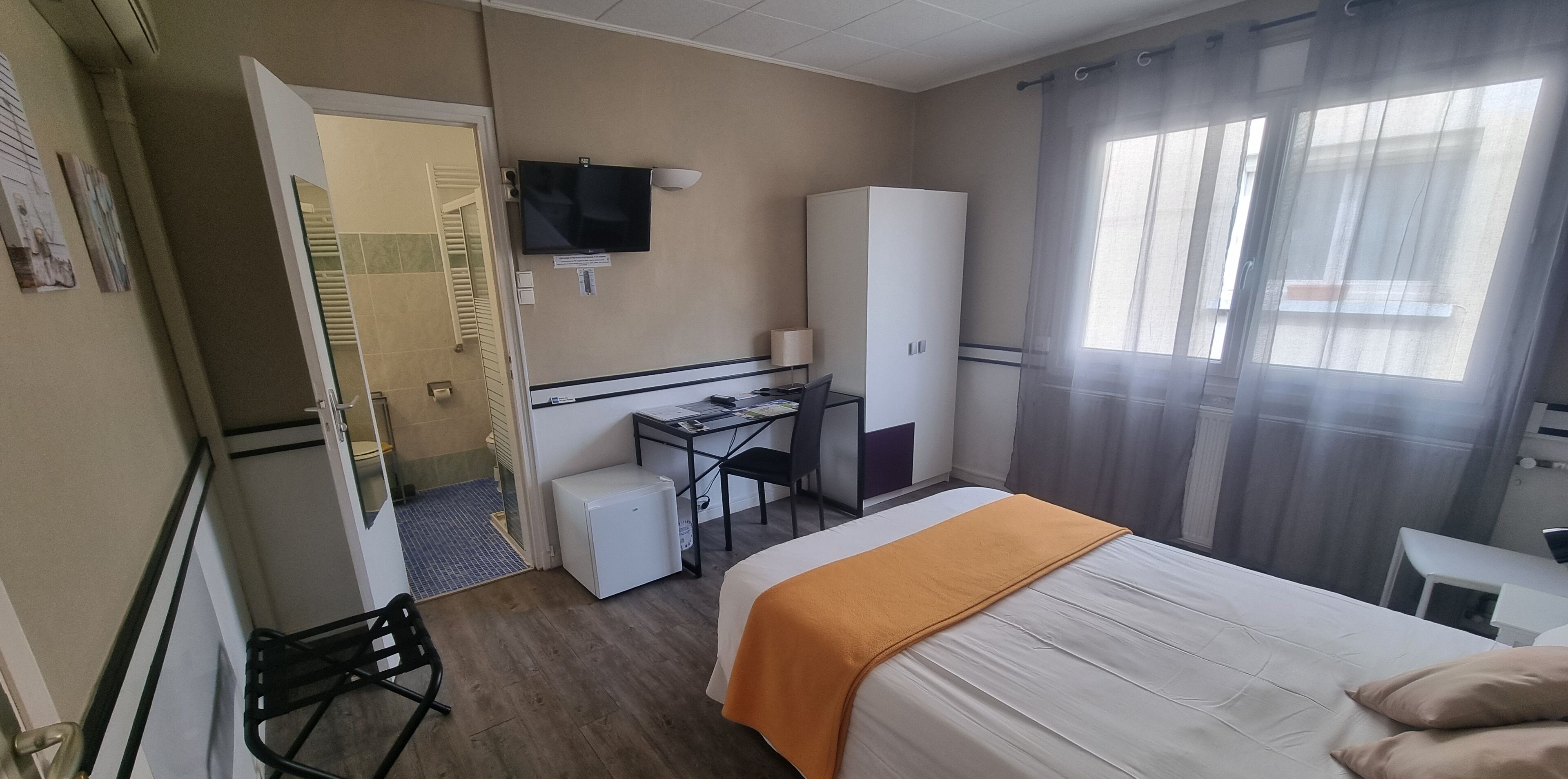 A hotel room with a bed, a desk, a television, a wardrobe, and a window with curtains.