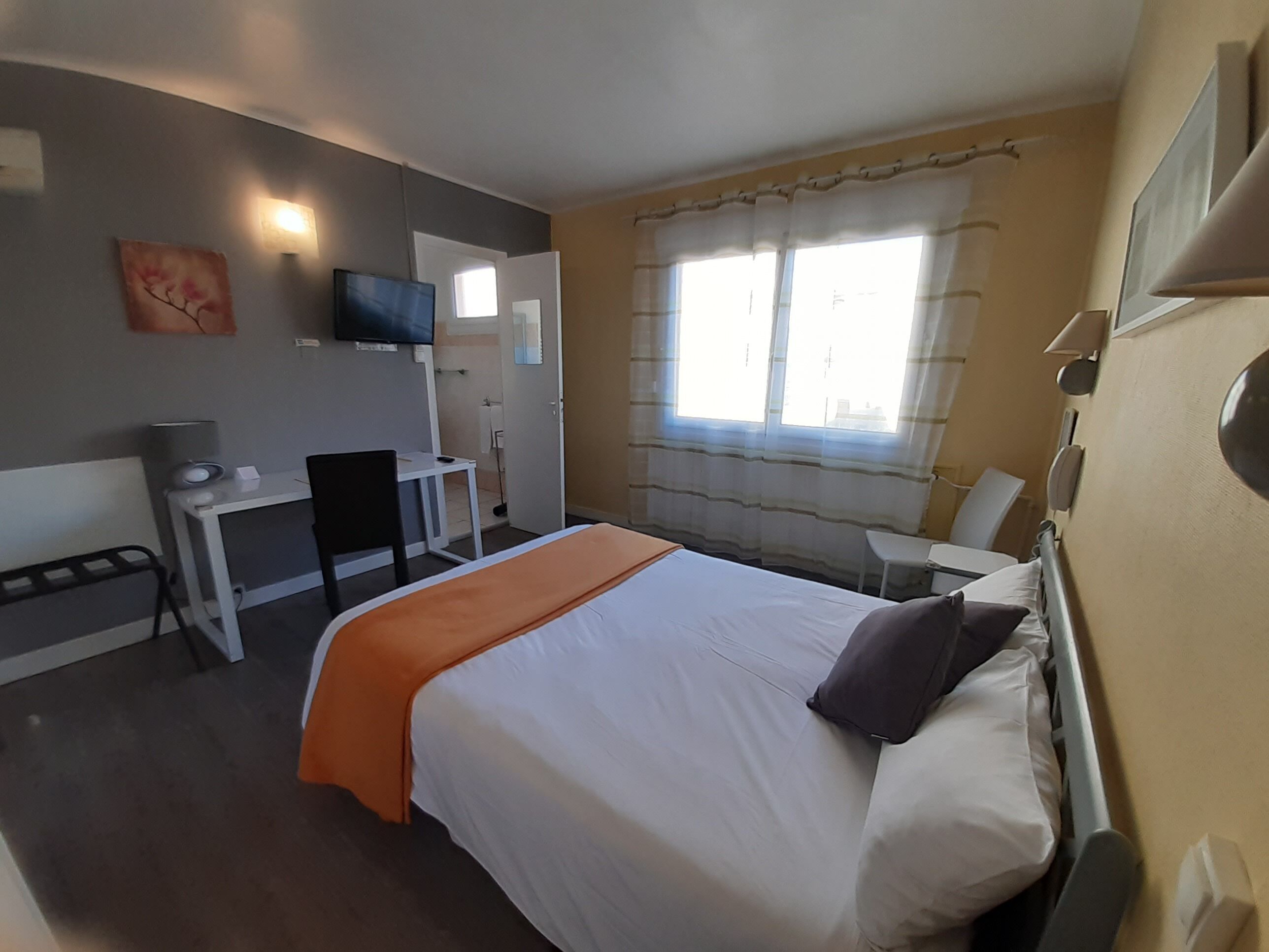 Habitación de hotel con cama, escritorio, silla, televisor y ventana con cortinas.