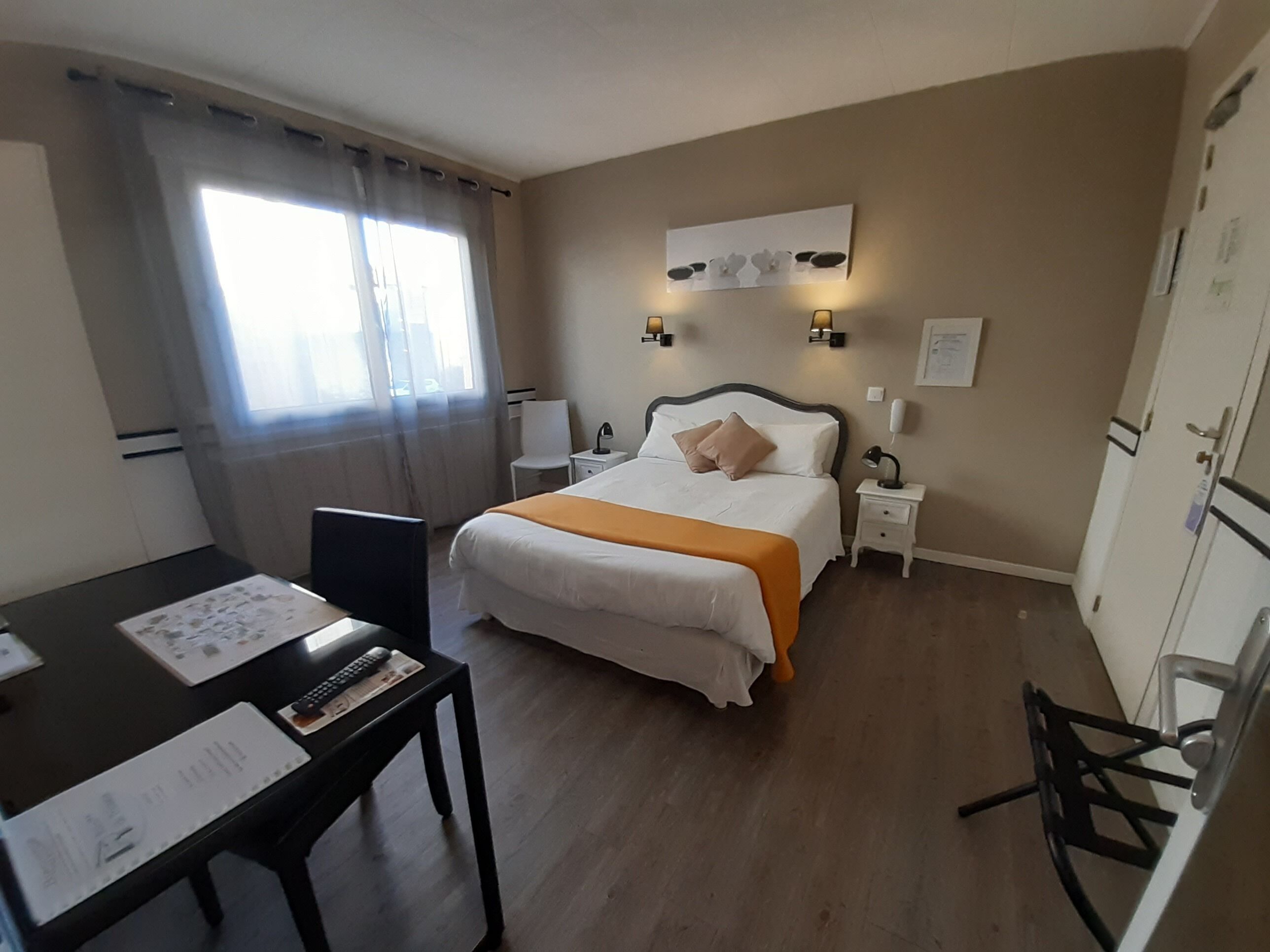 A hotel room with a bed, bedside tables, a desk with papers, a chair, and a window with curtains.