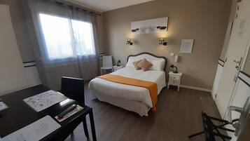 A hotel room with a bed, bedside tables, a desk with papers, a chair, and a window with curtains.