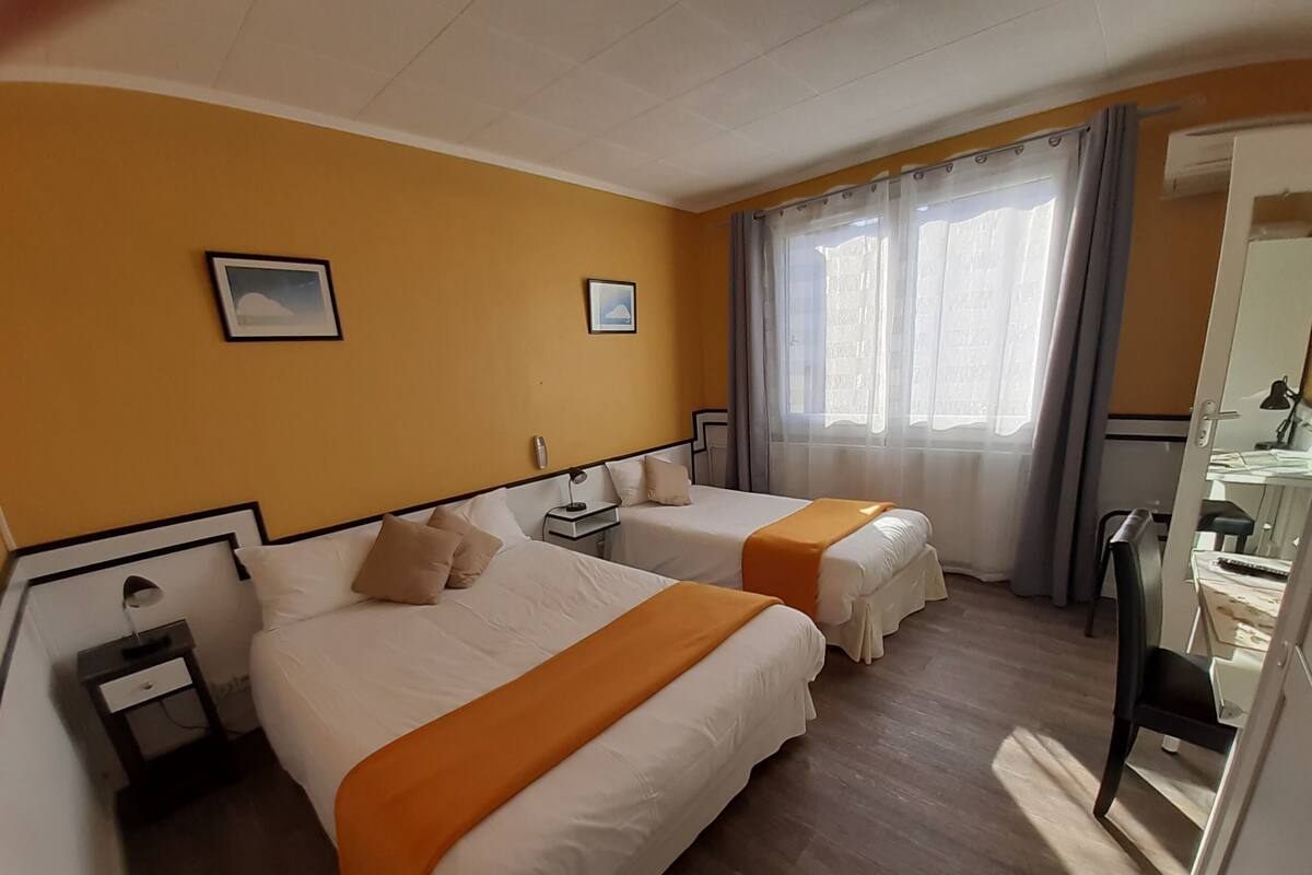 A hotel room with two beds, a desk, a chair, and a window with curtains.