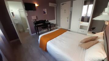Quarto de hotel com cama, escrivaninha, cadeira, guarda-roupa e televisão.