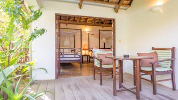 A wooden deck with a table and chairs, a bench, and a doorway leading to a room with a bed and a lamp.