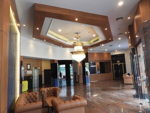 Un hall d’entrée spacieux avec un plafond haut, un lustre et un comptoir d’accueil.